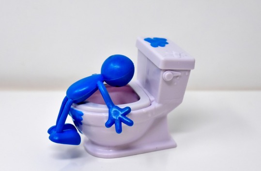 blue plasticine person leaning over a white toilet